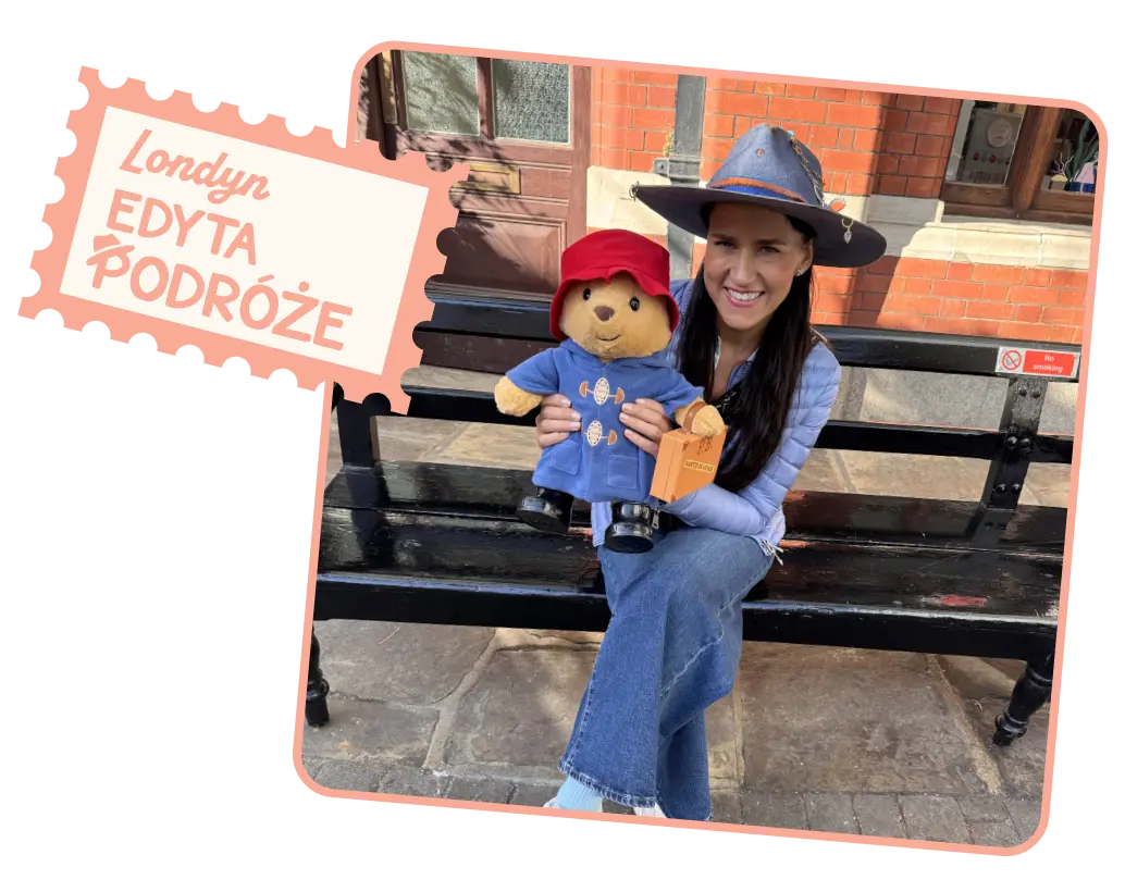 Organizatorka kobiecych wyjazdów Edyta Podróże uśmiecha się, siedząc na londyńskiej ławce z figurką misia Paddingtona.